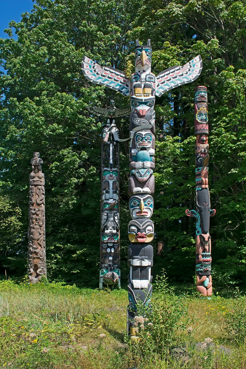 Totem pintado Kakaso'Las, no conjunto de totens do Stanley Park, em Vancouver, entre árvores.