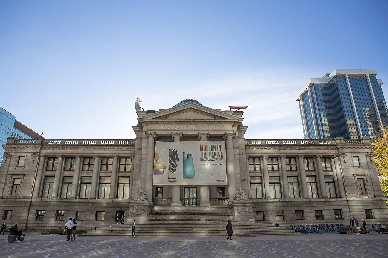 Fachada da Vancouver Art Gallery, com colunas, frontão, escadaria e um cartaz sobre a praça.