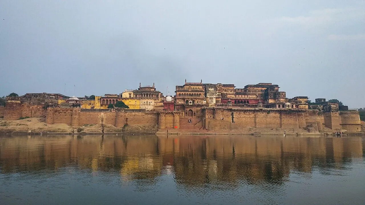 Muralha e palácios de arenito do forte de Ramnagar erguidos sobre a margem do Ganges, com escadarias descendo à água e o conjunto refletido no rio.