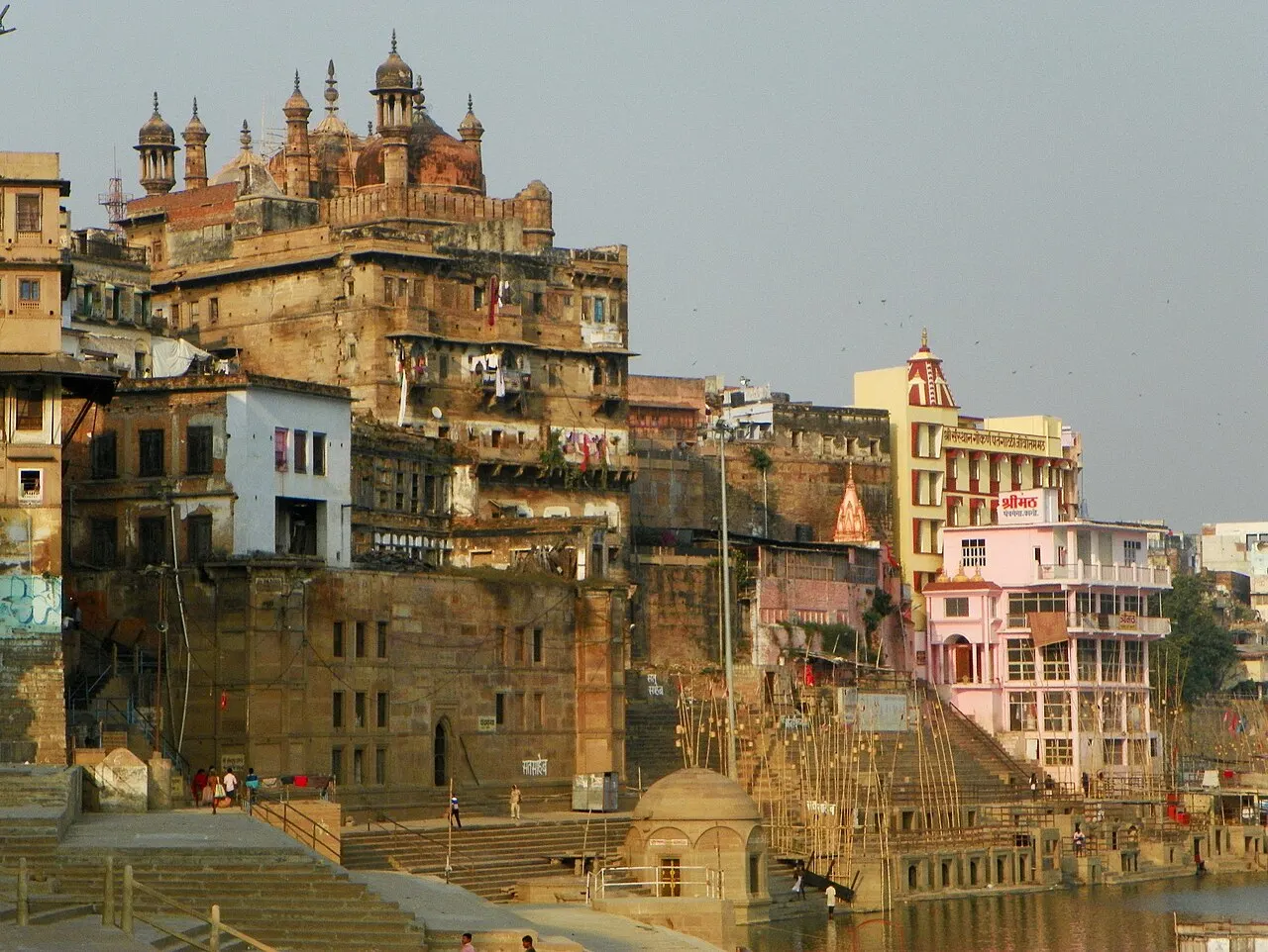Prédios antigos empilhados na margem do rio junto ao Panchganga Ghat, com torres e cúpulas ao alto.