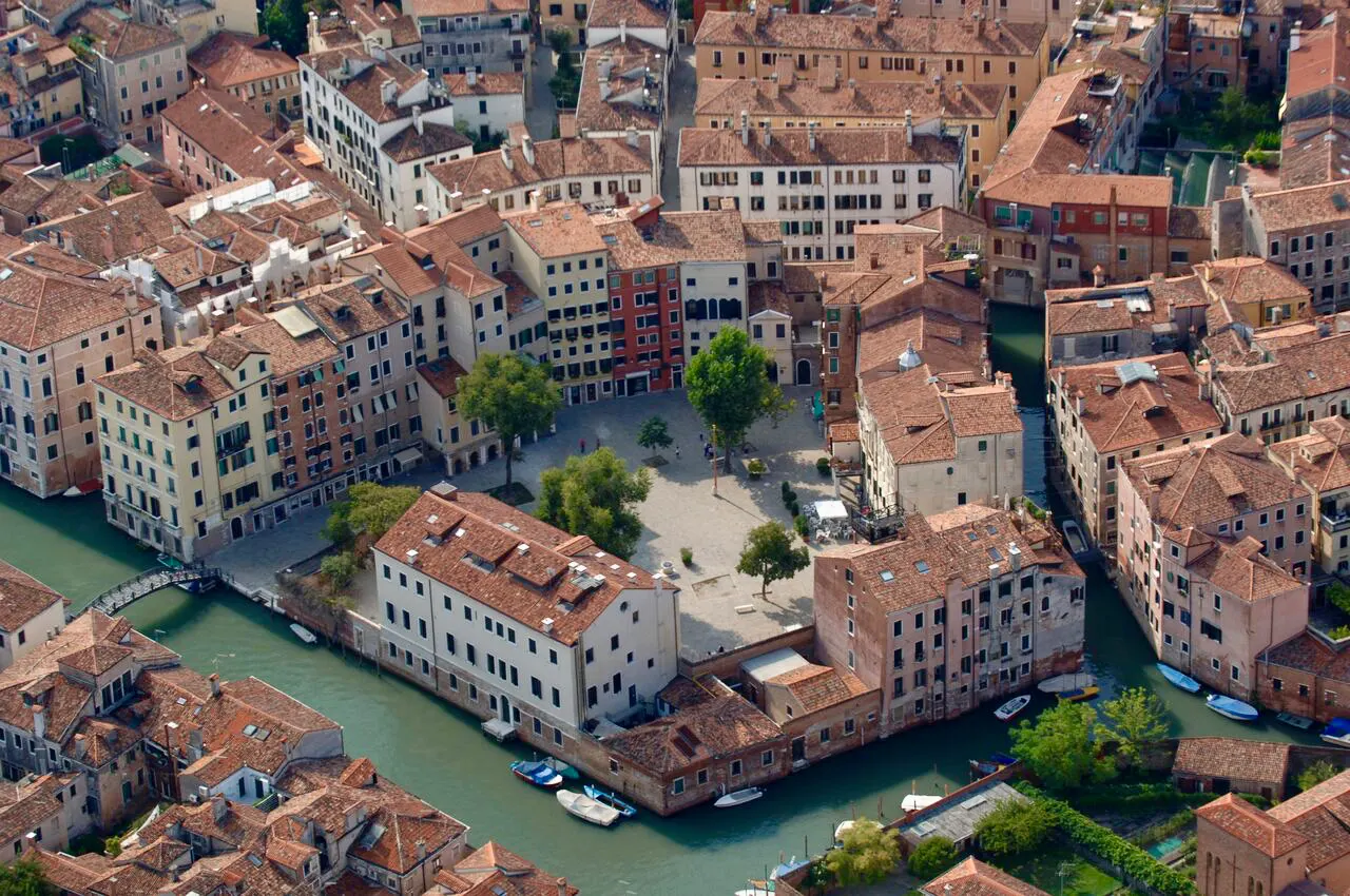 Vista aérea do Gueto de Veneza, com casas de telhados laranja, um canal e um campo aberto entre os prédios.