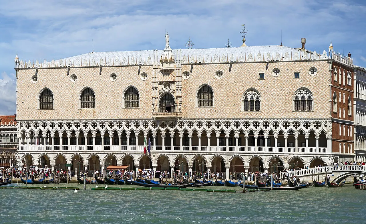 Fachada rosada em losangos do Palazzo Ducale, com arcada gótica de mármore branco e fileira de gôndolas ancoradas na água em frente.