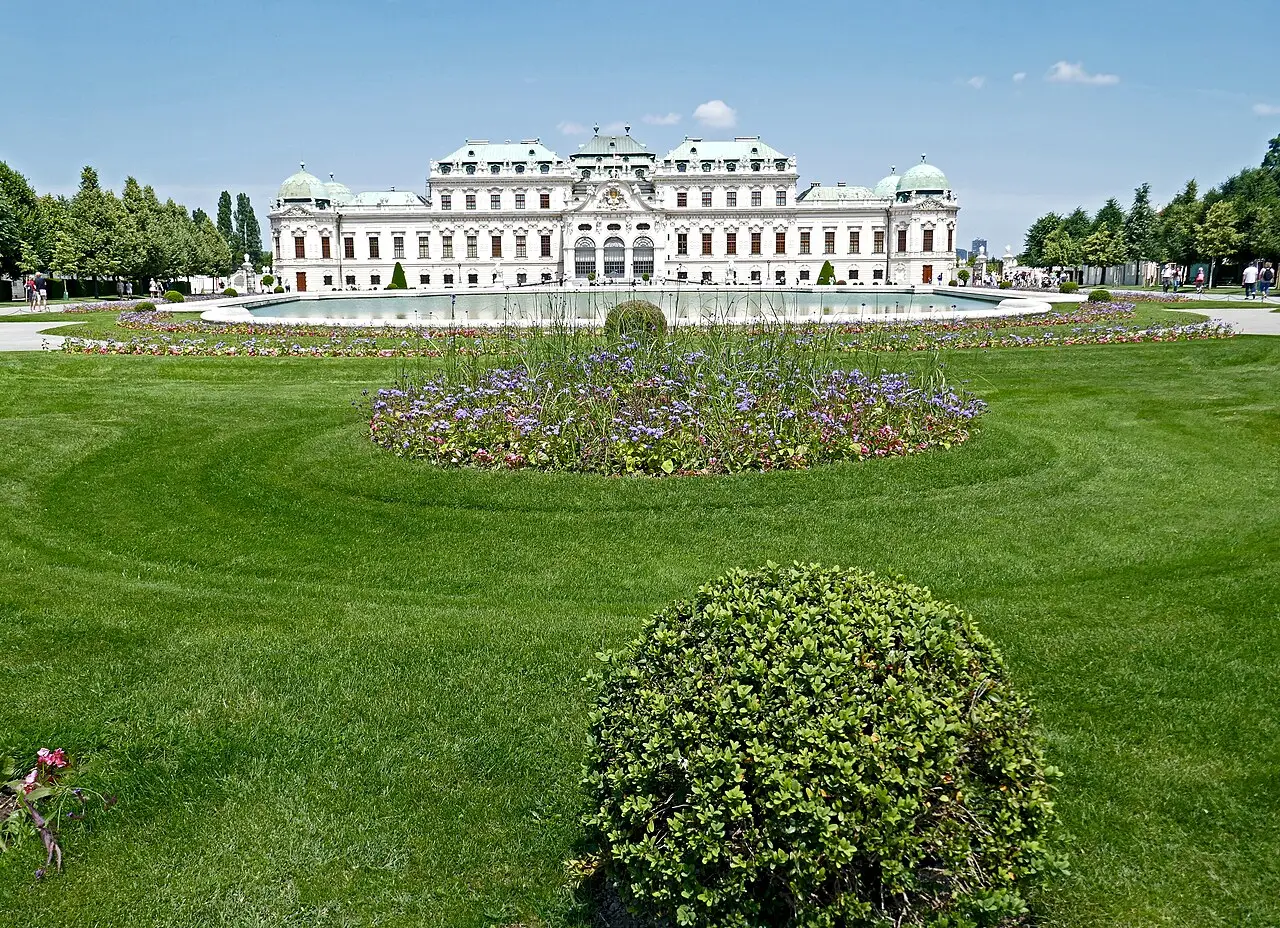Palácio do Belvedere Superior, em Viena, branco com telhados verdes, atrás do gramado e dos canteiros do jardim.