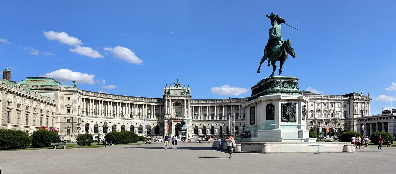 A bronze equestrian statue on a pedestal in Vienna's Heldenplatz, with the curved facade of the Neue Burg behind.