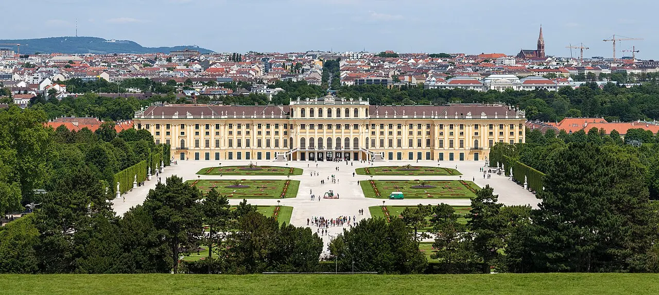 Palácio de Schönbrunn, em Viena, visto de longe, com os jardins em frente e a cidade ao fundo.