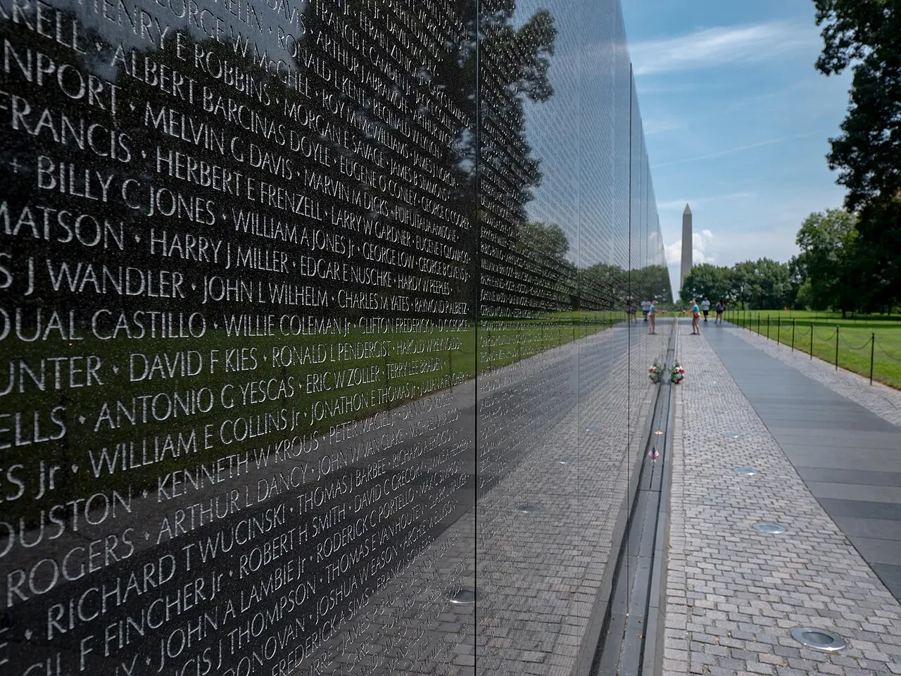 Le mur de granit noir du Vietnam Veterans Memorial, avec des noms gravés et le Washington Monument au fond.
