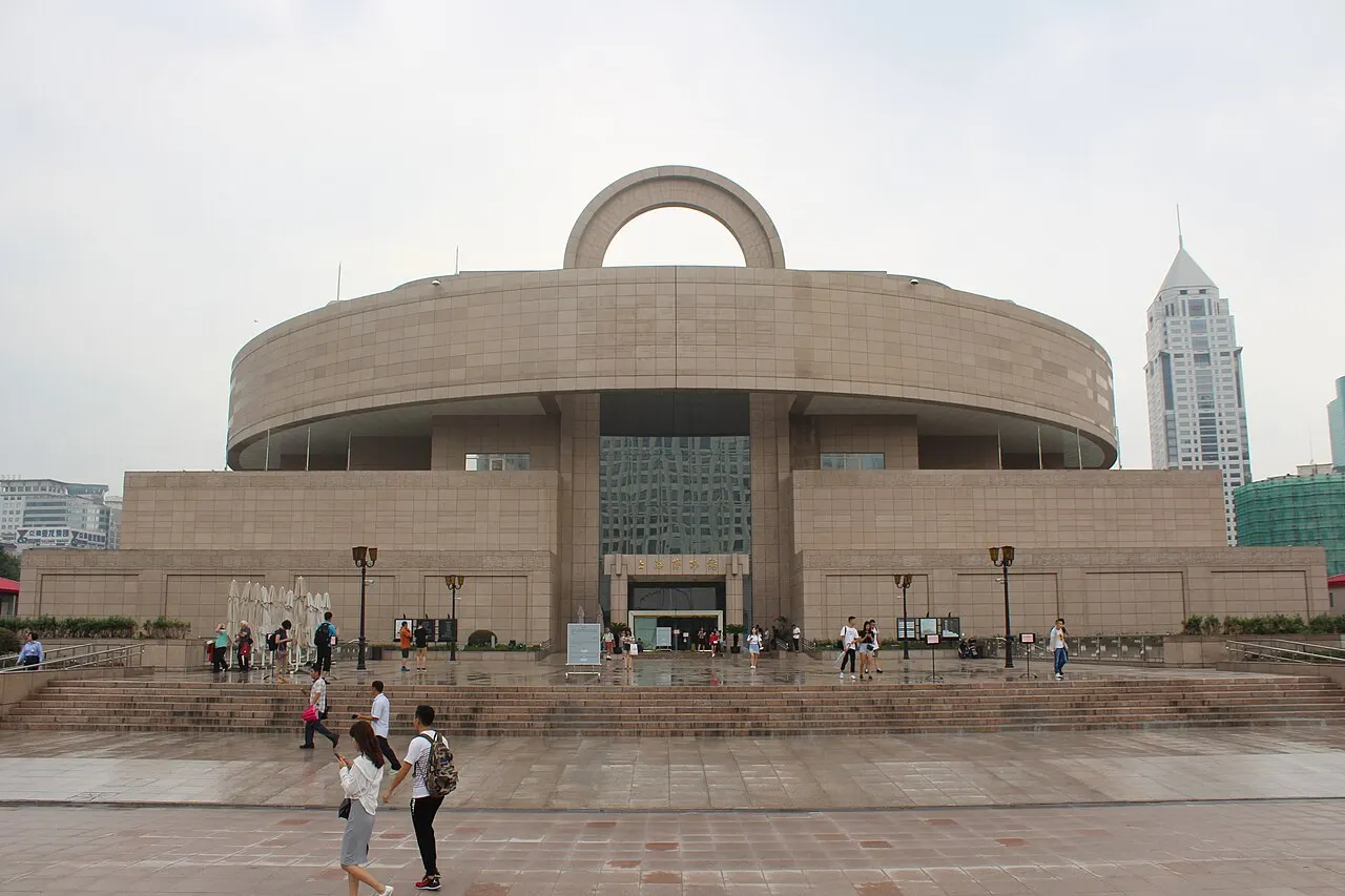 Prédio bege e redondo do Museu de Xangai, com base retangular e alça no topo.