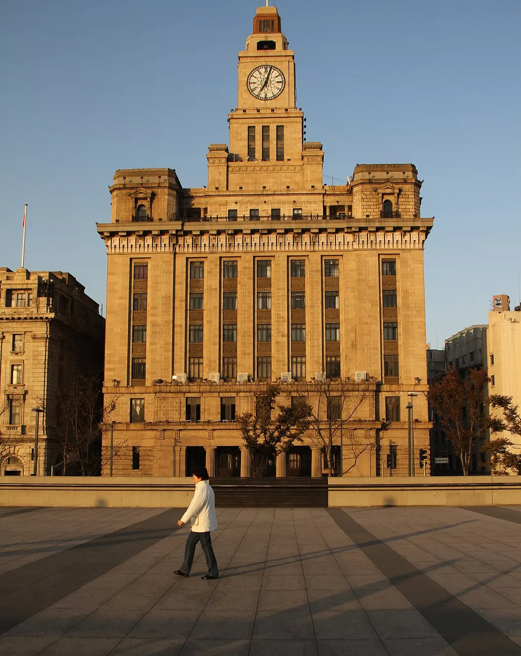 Prédio bege de estilo neoclássico com torre de relógio quadrada, na fileira de fachadas do Bund.