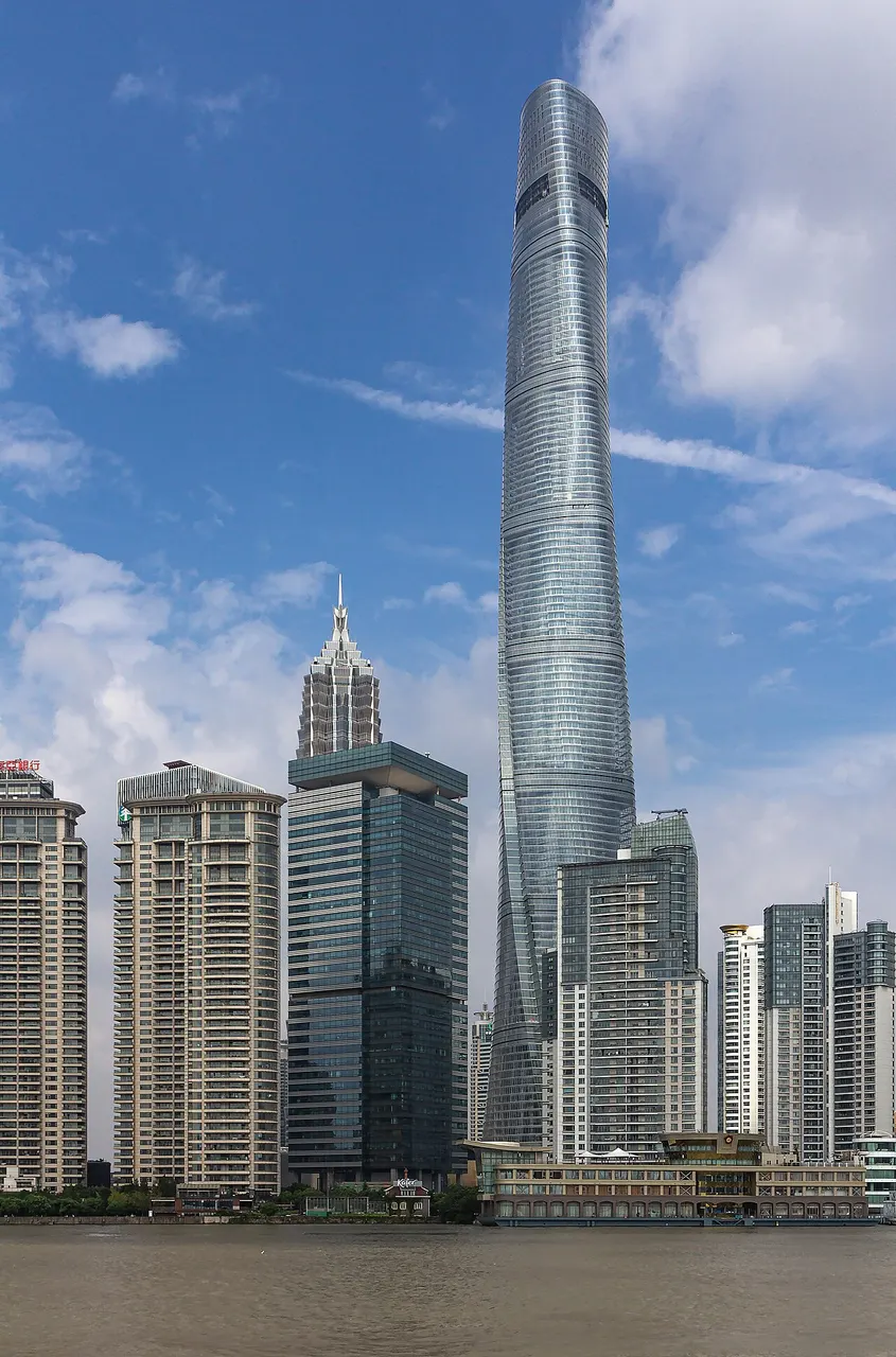 Torre de vidro azulado que se torce ao subir, mais alta que os prédios ao redor.