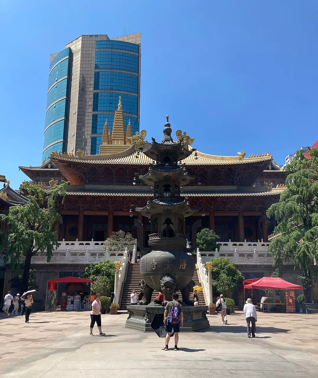 O Templo Jing'an, dourado, com telhados sobrepostos, ornamentos no topo e um arranha-céu ao fundo.