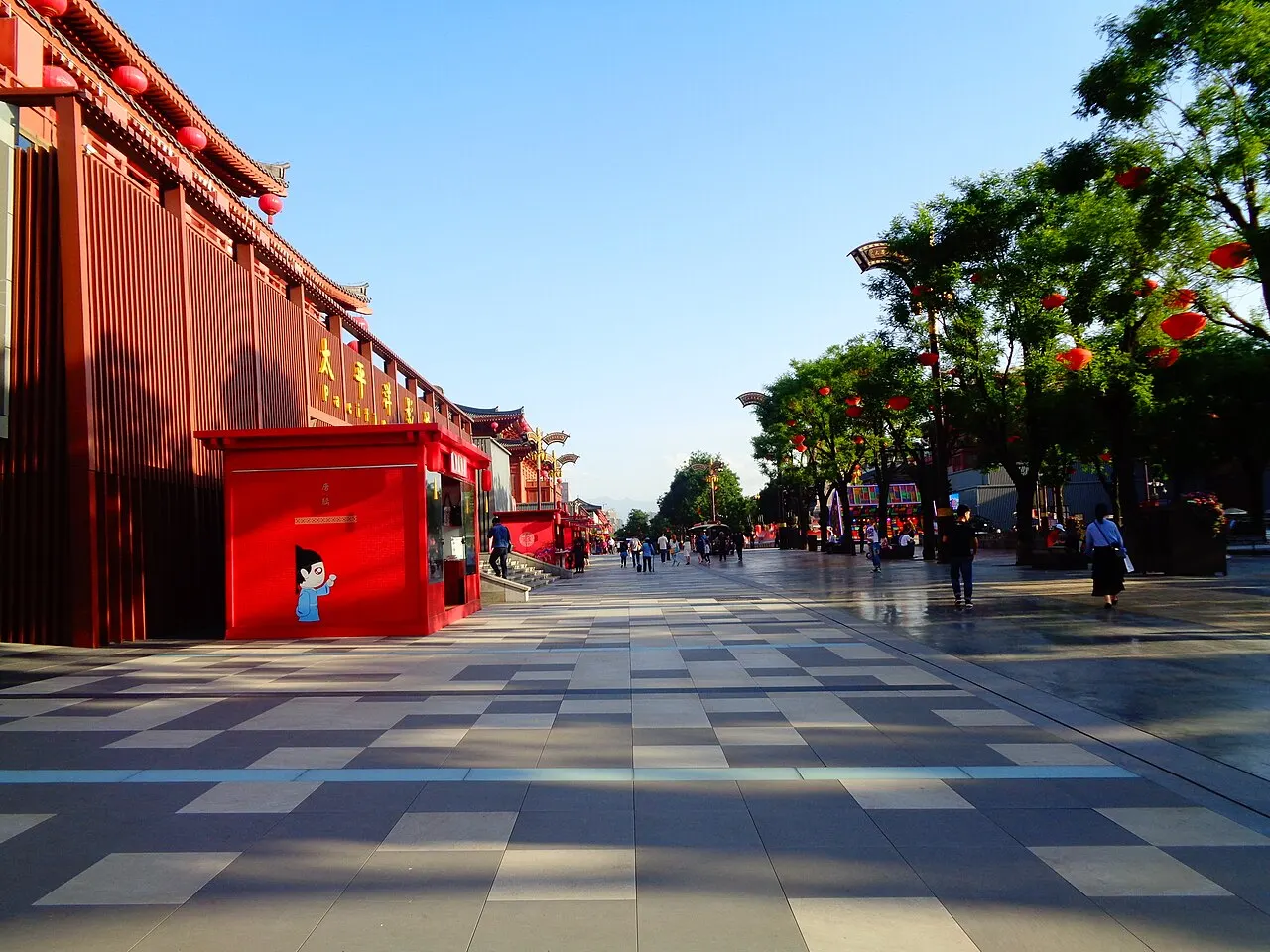 The Datang Everbright City pedestrian street in late-afternoon light, with a broad chequered pavement, red Tang-style facades on the left and red lanterns in the trees.