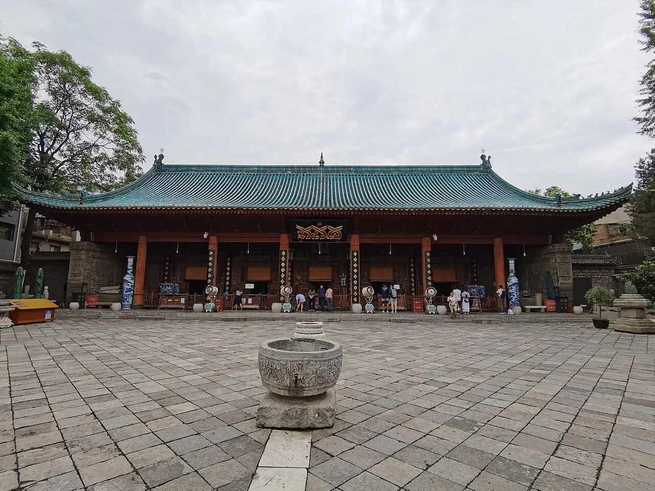 The prayer hall of the Great Mosque of Xi'an, a wooden pavilion with a green-tiled roof and red columns, facing a broad stone courtyard with a stone basin in the middle.