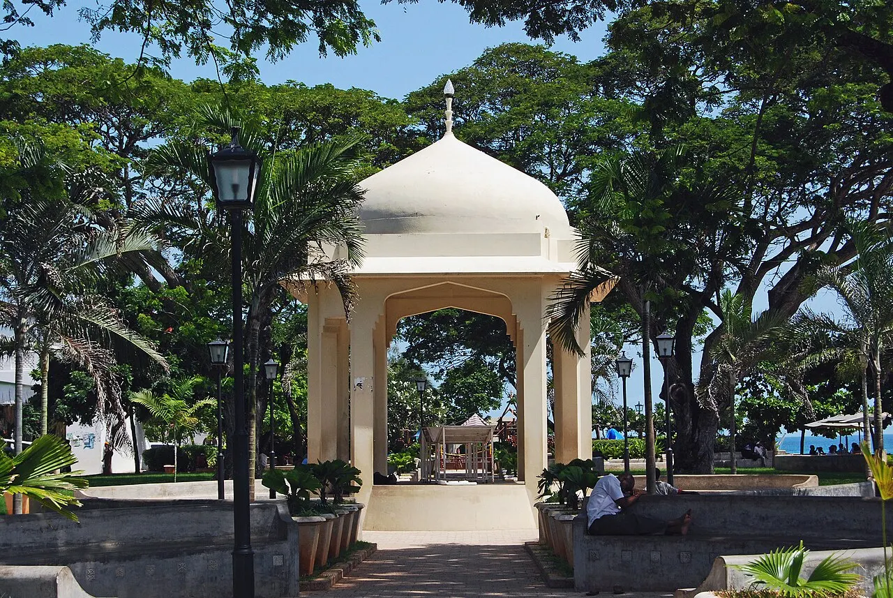 Pavilhão branco de cúpula nos Jardins de Forodhani, em Stone Town, entre árvores.