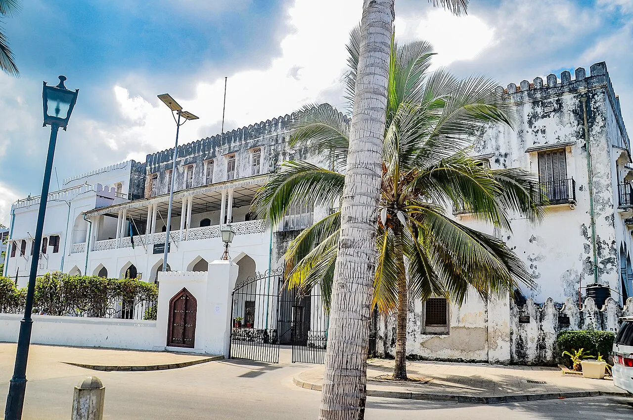 Fachada branca do antigo palácio do sultão, hoje museu, com varandas, uma palmeira e um poste de rua à frente.