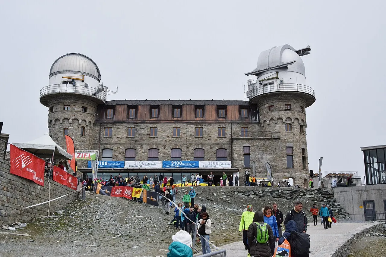 O prédio de pedra do Gornergrat com as duas cúpulas de observatório, num dia de prova de corrida, com faixas e pessoas na frente.
