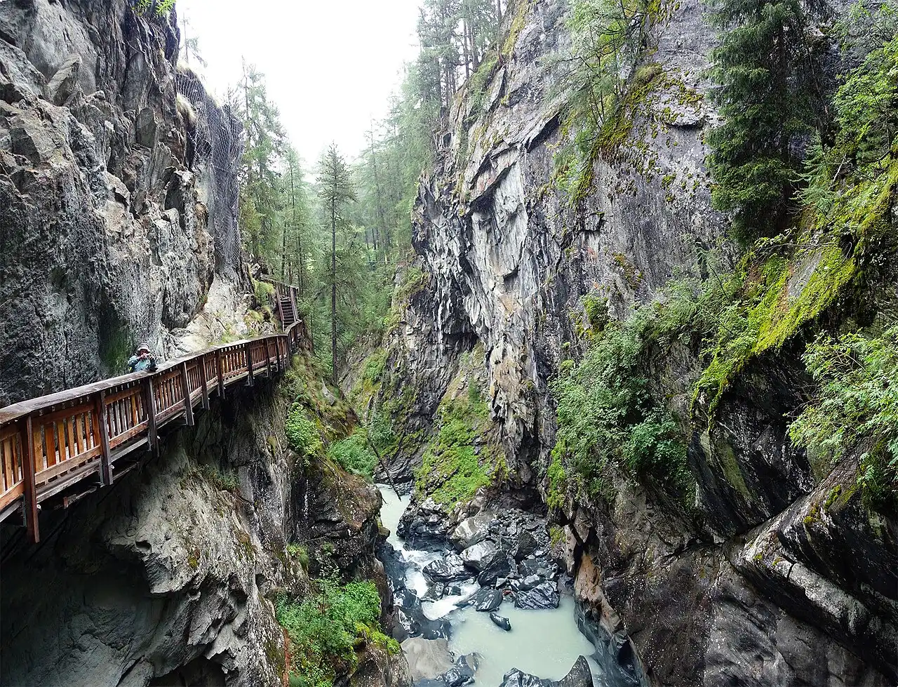 A garganta de Gorner com paredes de rocha cobertas de musgo, o rio claro embaixo e uma passarela de madeira presa à pedra.