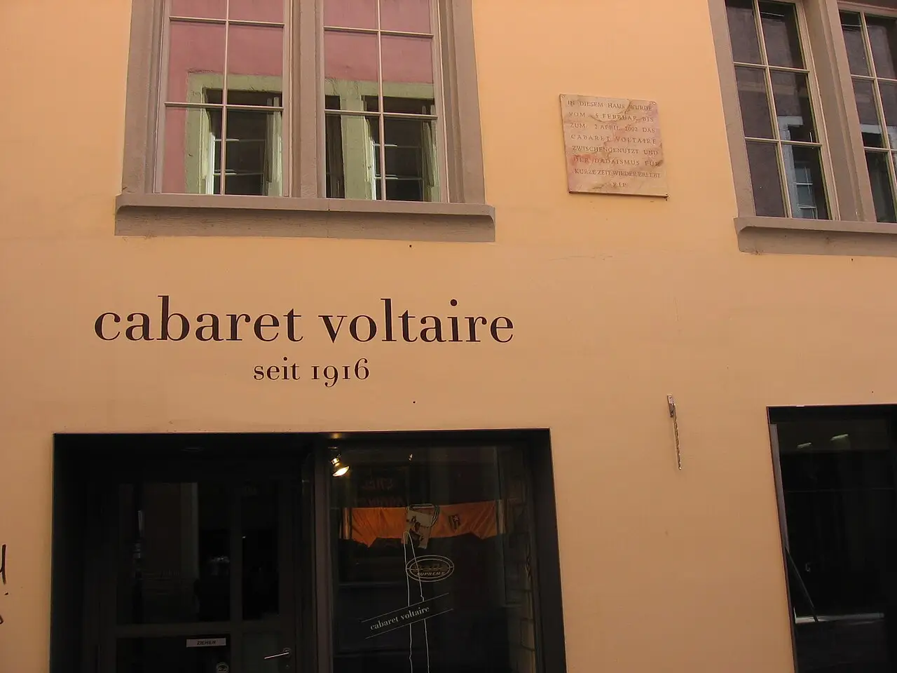 Fachada do Cabaret Voltaire, com a inscrição cabaret voltaire seit 1916, duas janelas e a porta de vidro.