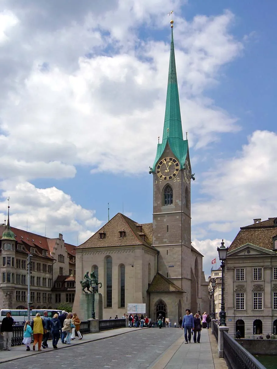 Fraumünster, em Zurique, com a torre fina de agulha verde sob céu com nuvens.