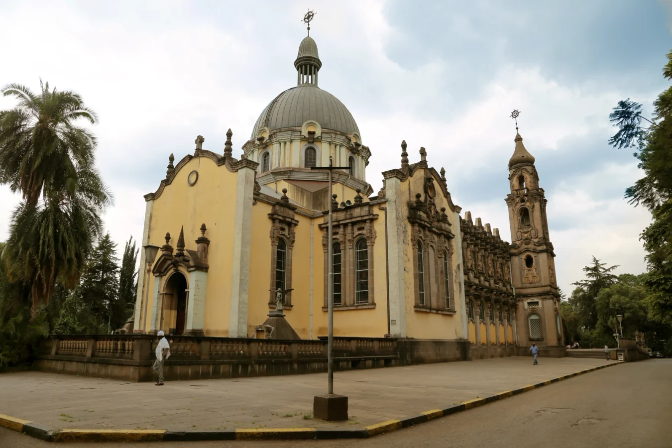Catedral da Santíssima Trindade vista de lado, com cúpula e torre inteiras, palmeiras à esquerda e o pátio em primeiro plano.