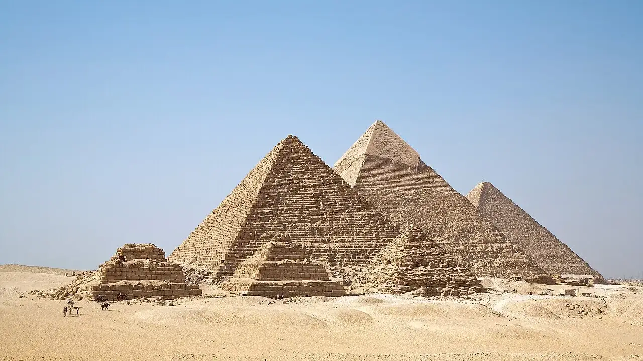 As três pirâmides de Gizé, no Egito, com as pirâmides menores das rainhas à frente, sobre a areia.