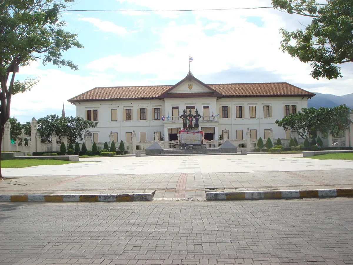 Monumento aos Três Reis diante do Centro de Artes e Cultura de Chiang Mai, com árvores em primeiro plano e montanha distante; fotografia de 2009.