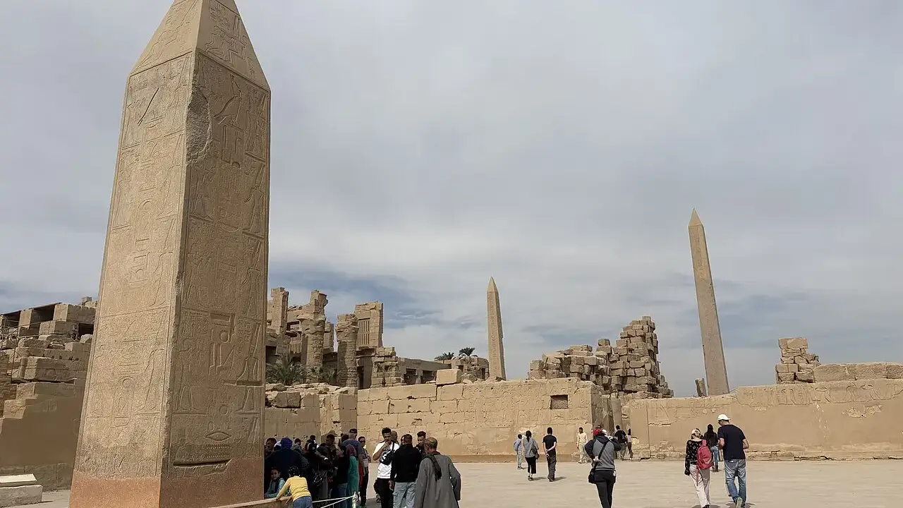 Obelisco de granito no complexo de Karnak, em Luxor, com visitantes pequenos ao pé.