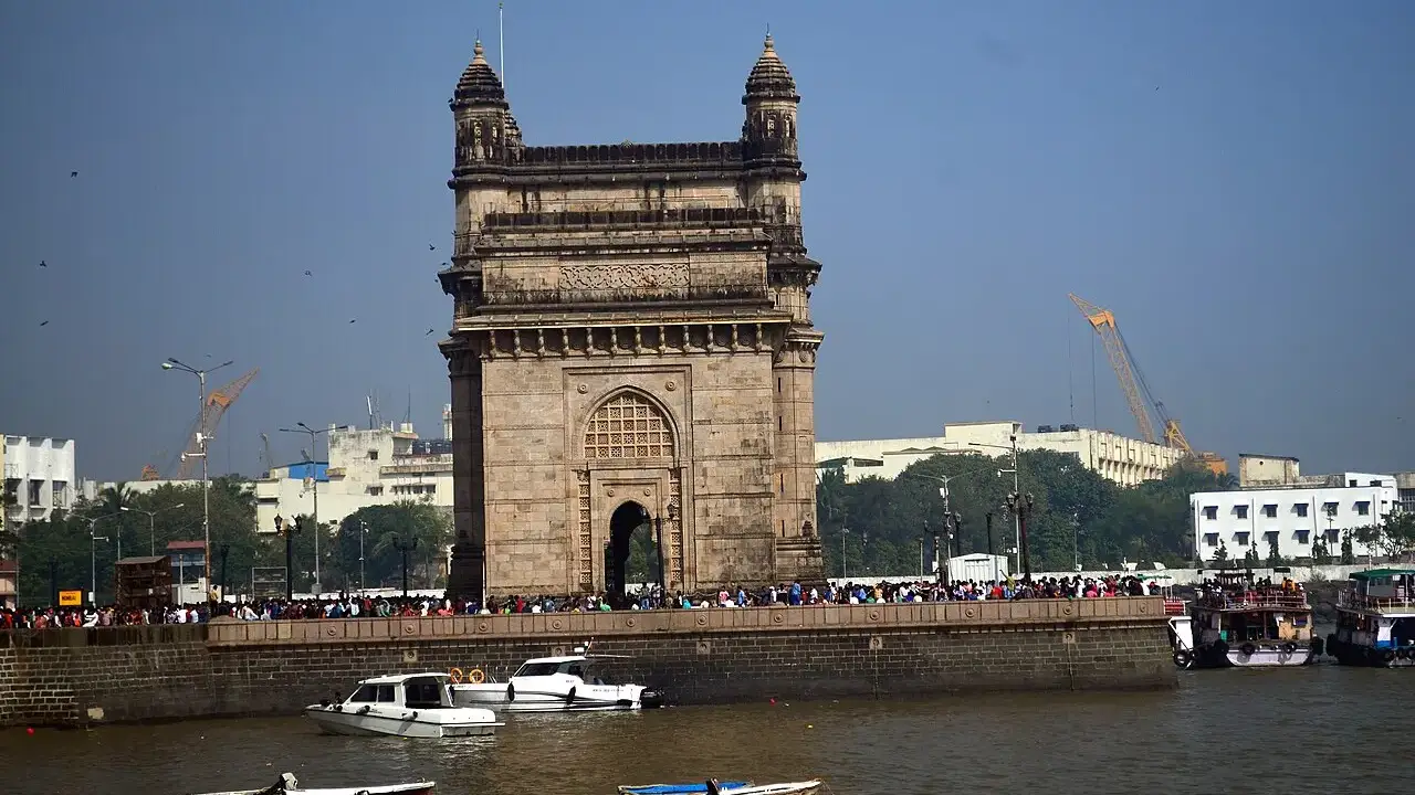 Arco monumental de pedra basáltica amarelada, com quatro torres, à beira da água.