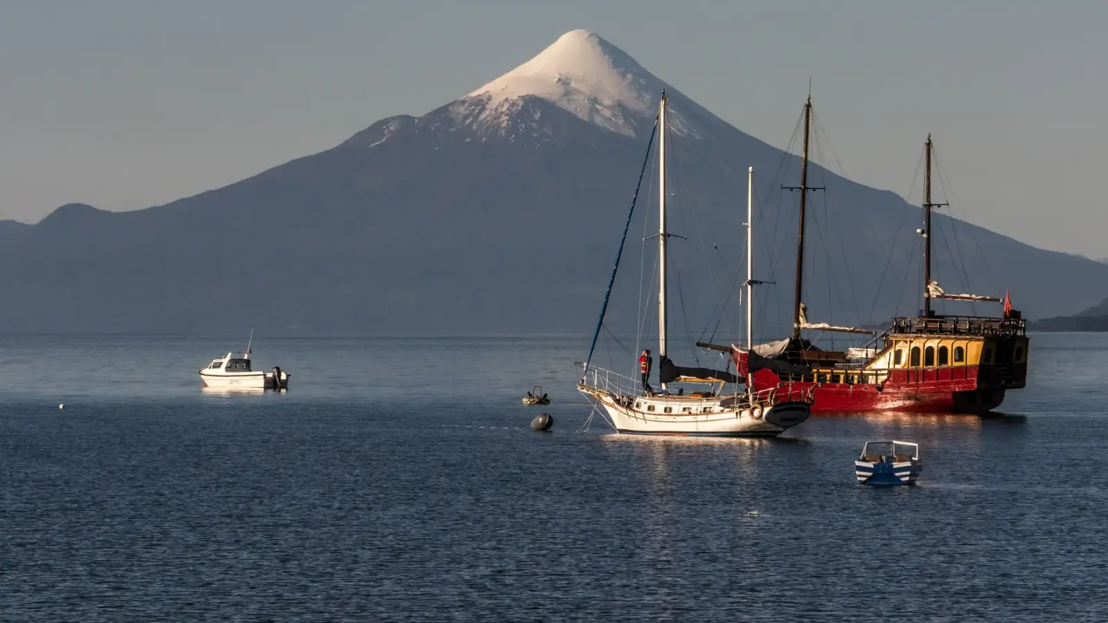 O cone nevado do vulcão Osorno sobre o Lago Llanquihue, com veleiros e pequenos barcos ancorados diante de Puerto Varas.
