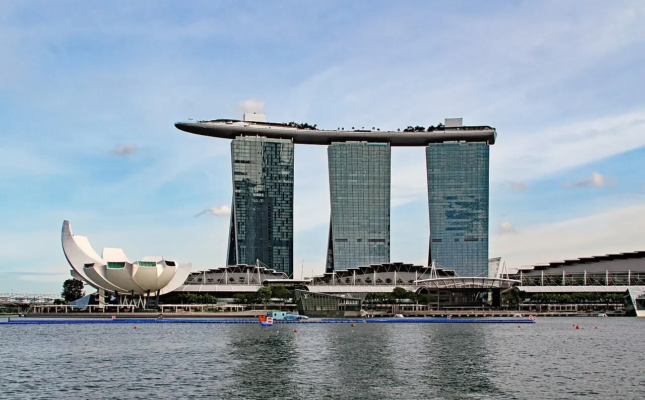 Marina Bay Sands e ArtScience Museum à margem da baía de Singapura, com torres e SkyPark inteiros, cabos e pontão/barco frontais sobre a água.
