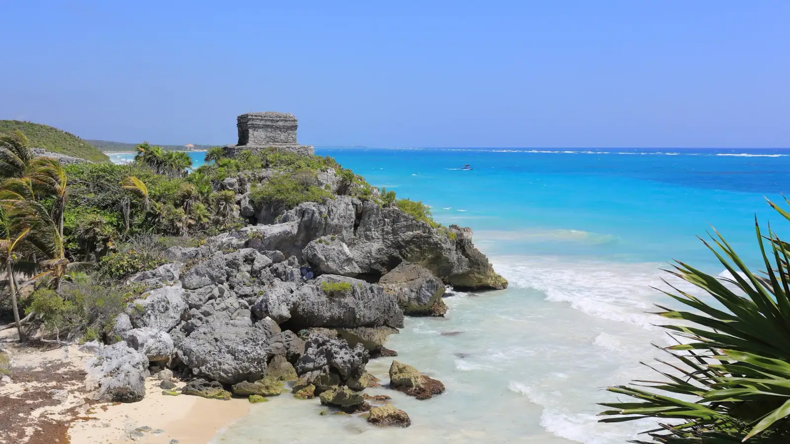 Templo do Vento sobre a falésia de Tulum, com mar azul ao fundo e folhas de agave em primeiro plano; fotografia de março de 2016.