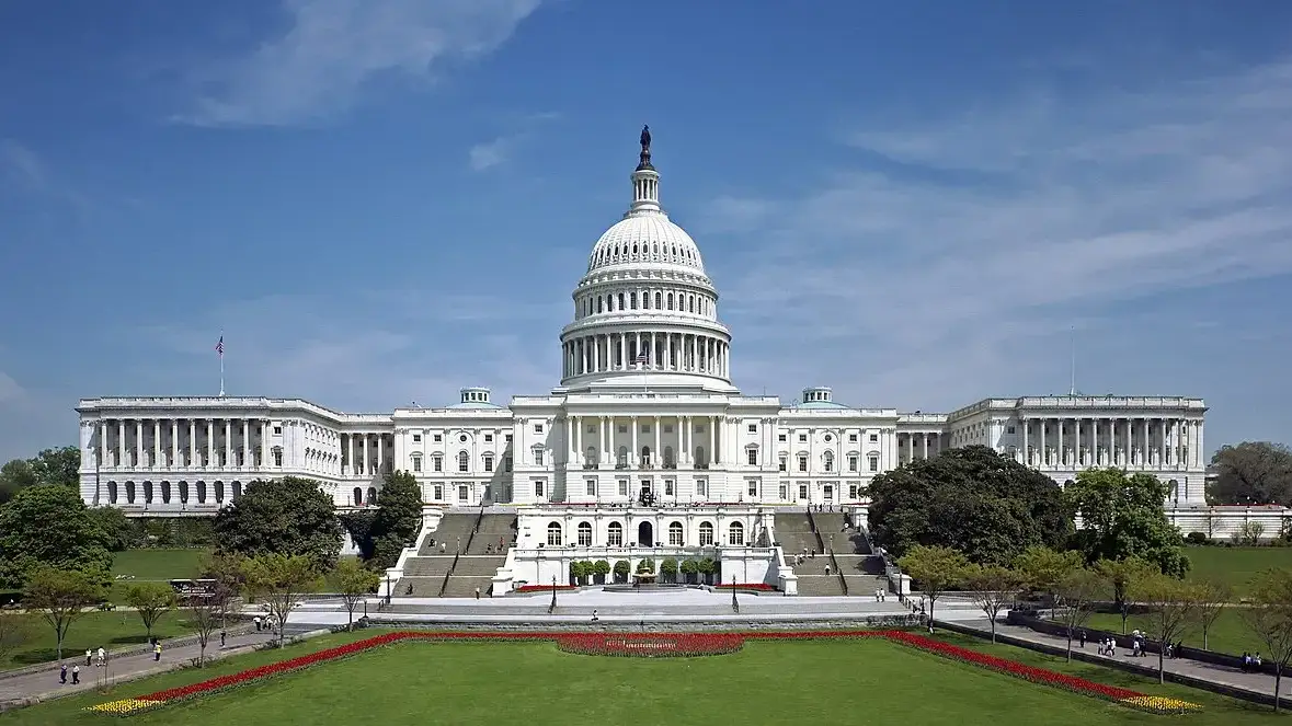 Fachada oeste do Capitólio dos Estados Unidos, com a cúpula branca e os terraços, sob céu azul.