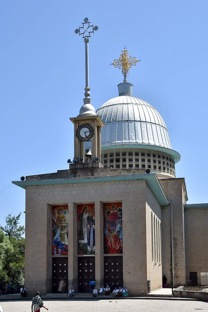 Igreja de pedra com cúpula de metal, cruz no alto e vitrais na fachada, sob céu azul.