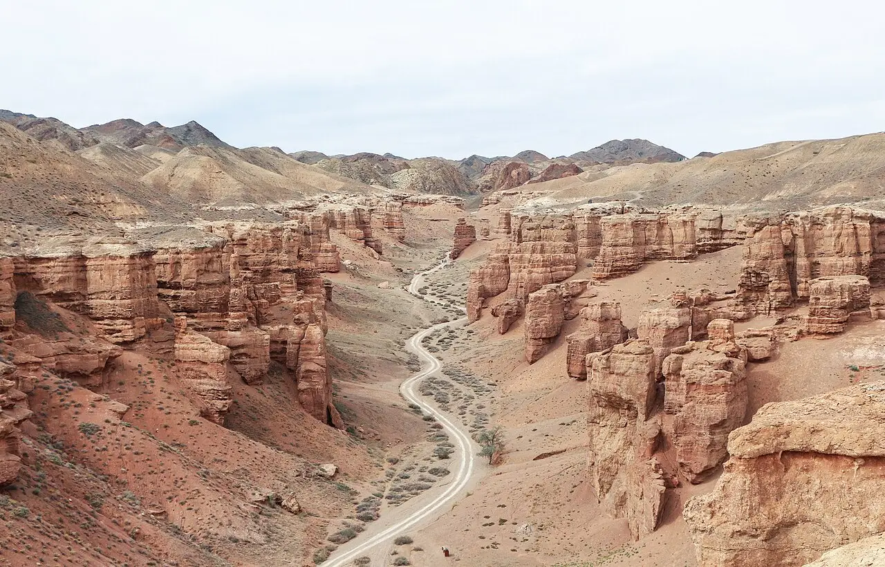 Vale do Cânion de Charyn, com formações de arenito avermelhado dos dois lados e uma estrada de terra sinuosa no fundo.