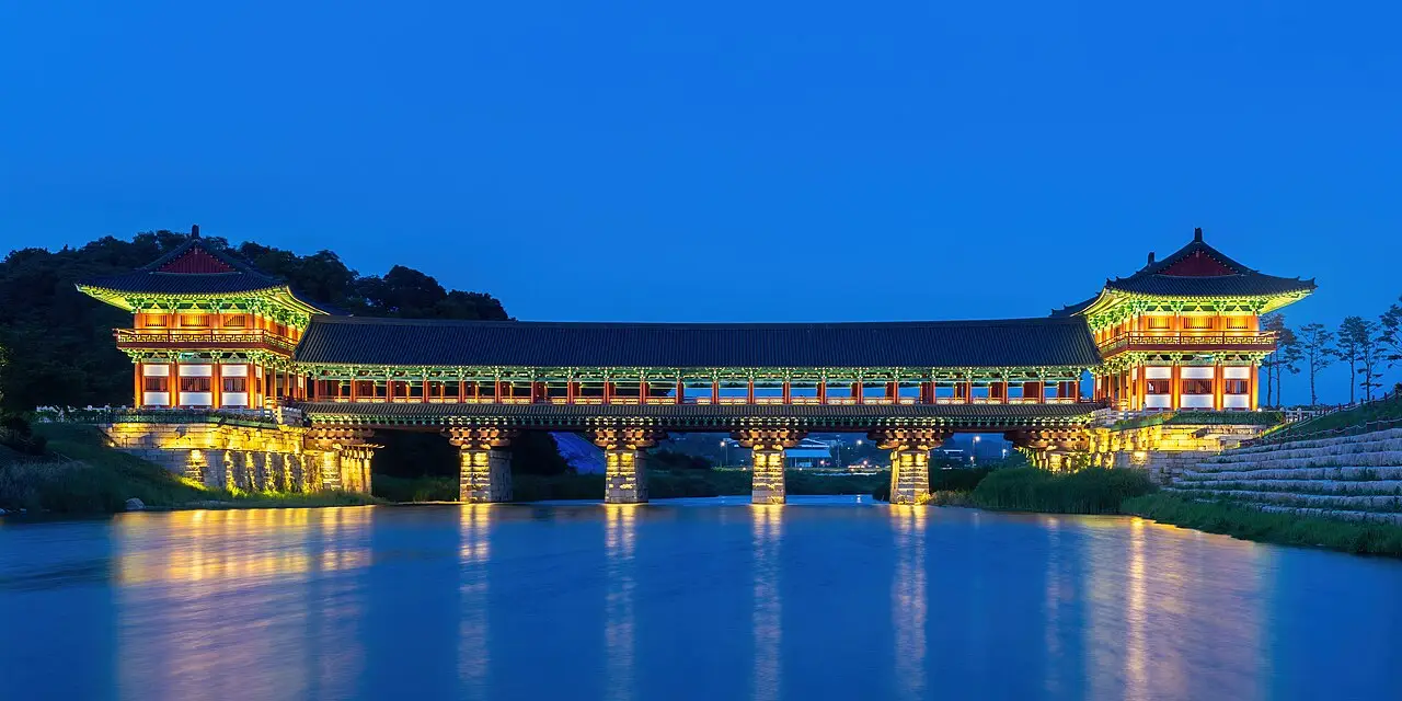 Ponte Woljeonggyo iluminada ao anoitecer em Gyeongju, uma ponte coberta de madeira com dois pavilhões e o reflexo das luzes na água.