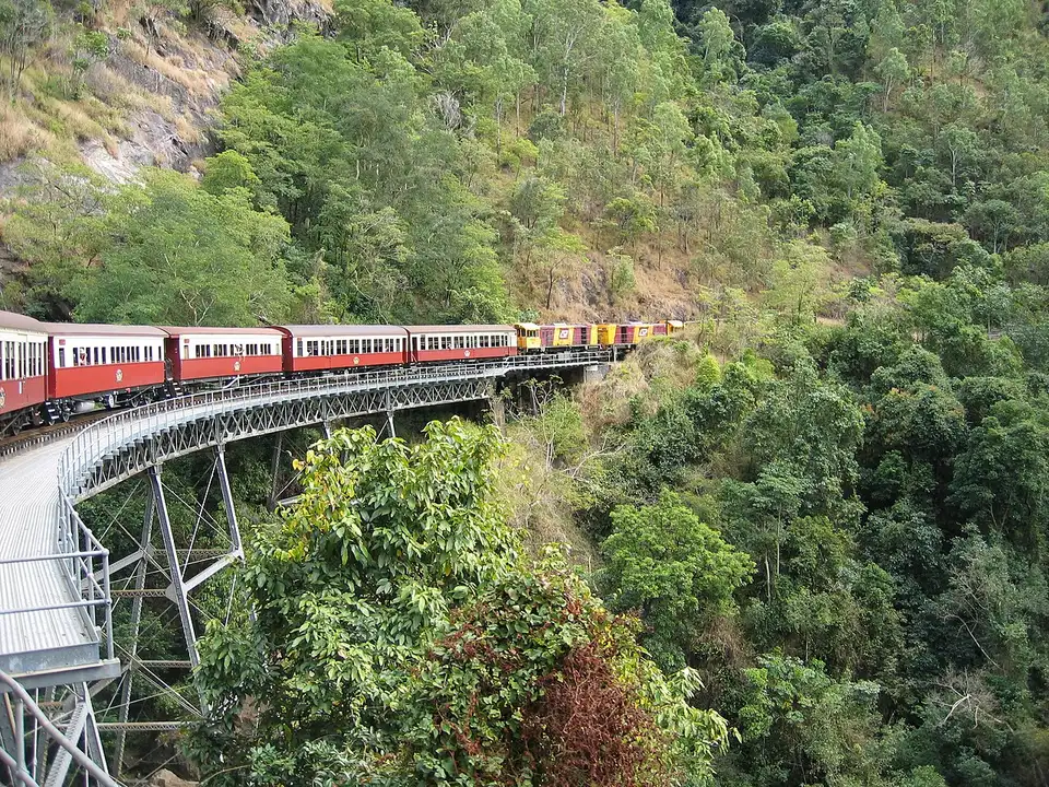 Train de voitures rouges et crème sur un pont d’acier au-dessus de la gorge verte de Barron.