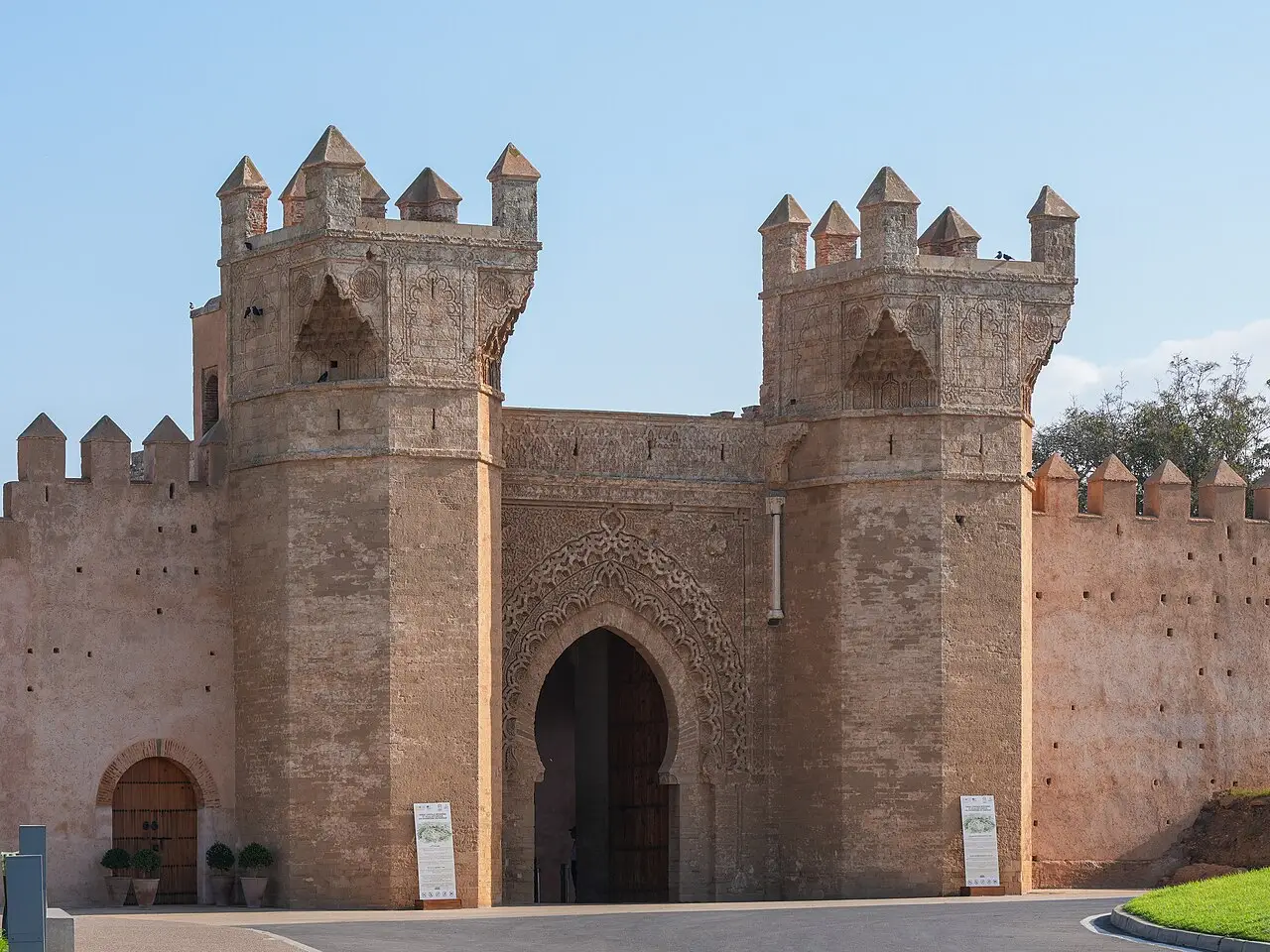 Portão principal de Chellah em Rabat, com duas torres octogonais de ameias, arco de ferradura decorado e muralha de tom rosado.
