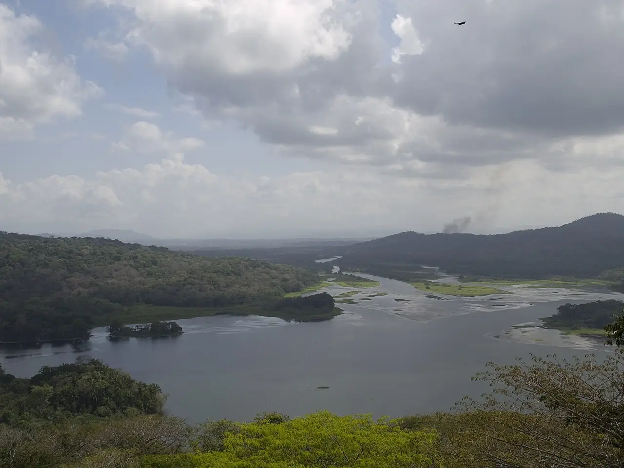 Vista do alto sobre a floresta tropical de Gamboa, com um rio largo entre morros cobertos de mata e nuvens no céu.
