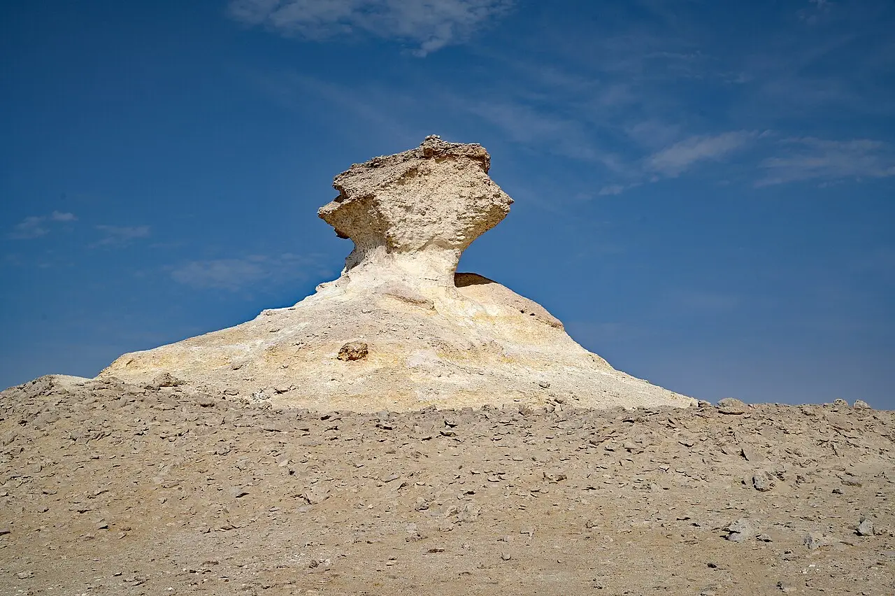 Formação rochosa de calcário claro em forma de cogumelo sobre uma colina no deserto da península de Zekreet, contra um céu azul.