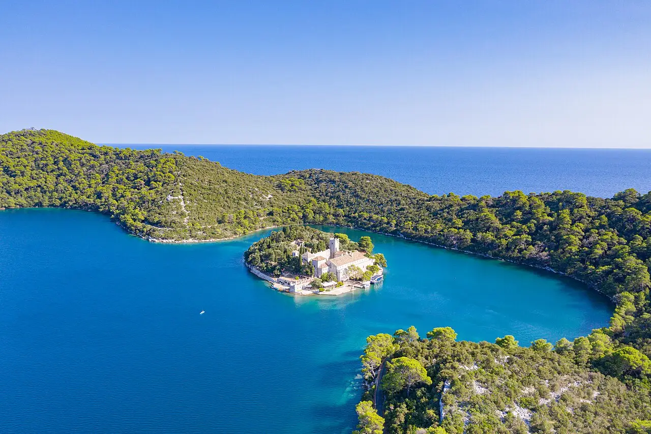 Vista aérea da pequena ilha de Santa Maria com o mosteiro, no meio de um lago azul cercado por colinas de pinheiros no Parque Nacional de Mljet.