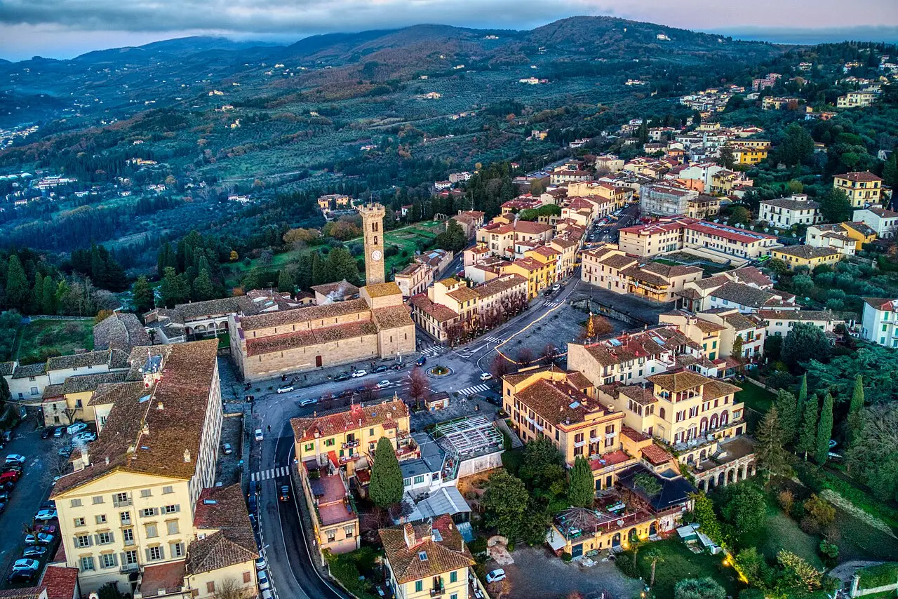 Vista aérea de Fiesole ao entardecer, com a Piazza Mino, a catedral de torre alta e casas de telhado de barro sobre colinas de oliveiras.