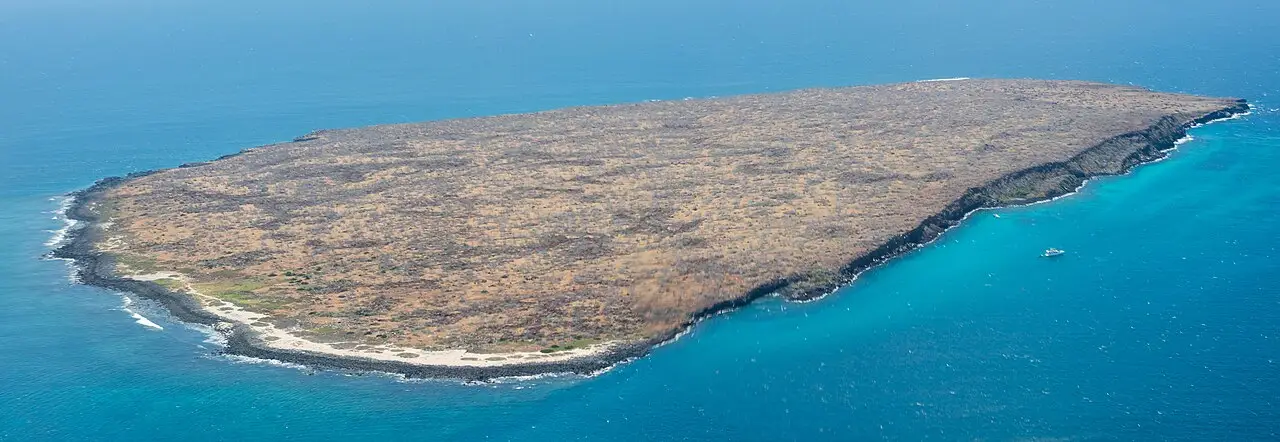 Ilha baixa e árida, de costa escura, cercada de mar azul.