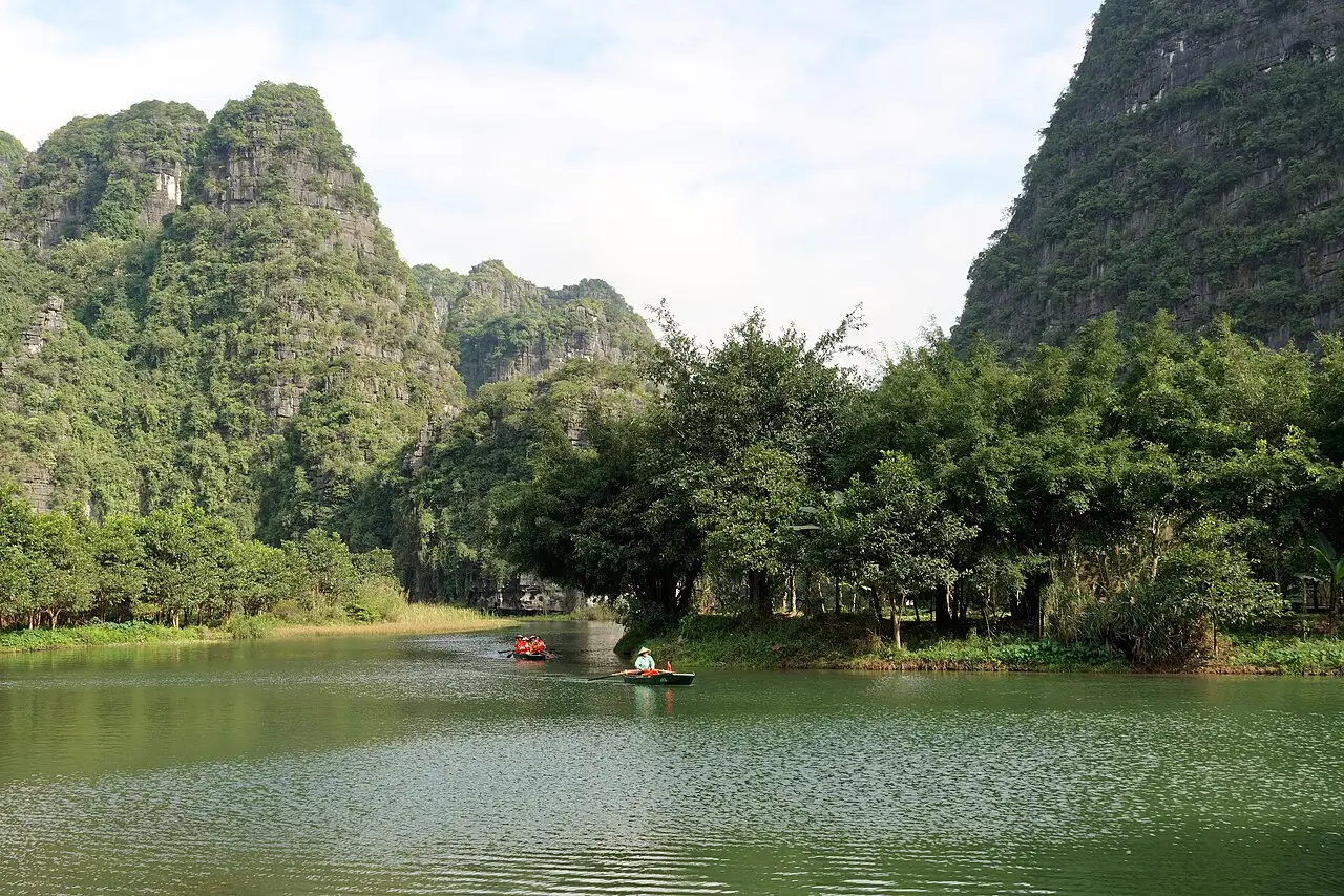 Barcos de remo em águas verdes entre morros de calcário cobertos de vegetação no complexo paisagístico de Tràng An, na província de Ninh Bình.