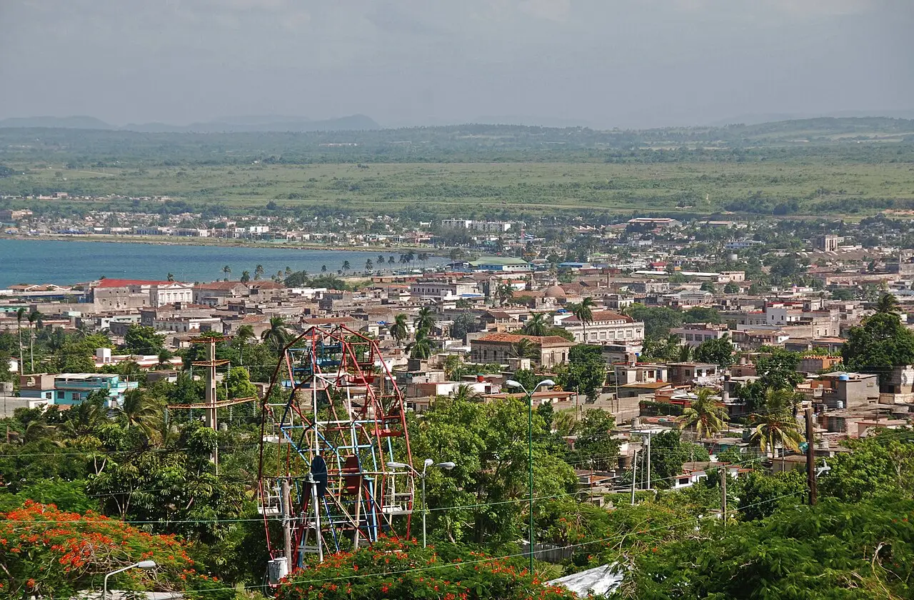 Vista do alto da cidade de Matanzas, com telhados e palmeiras em primeiro plano, a baía à esquerda e uma planície verde até o horizonte.