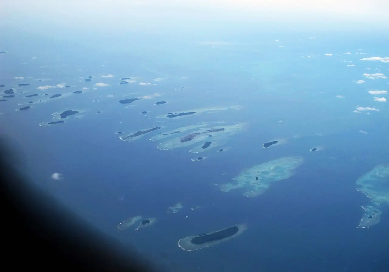 Dezenas de ilhas baixas espalhadas no mar azul, vistas de um avião.