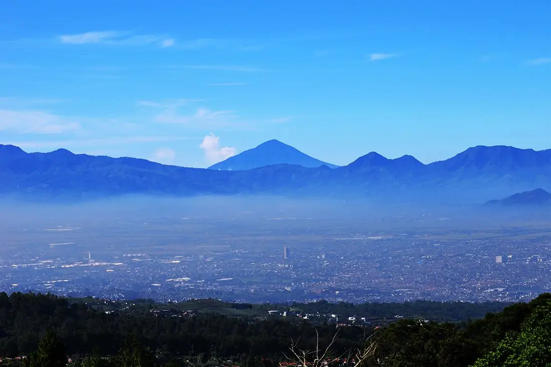 A cidade no fundo de um vale, com vulcões azuis atrás, sob céu limpo.