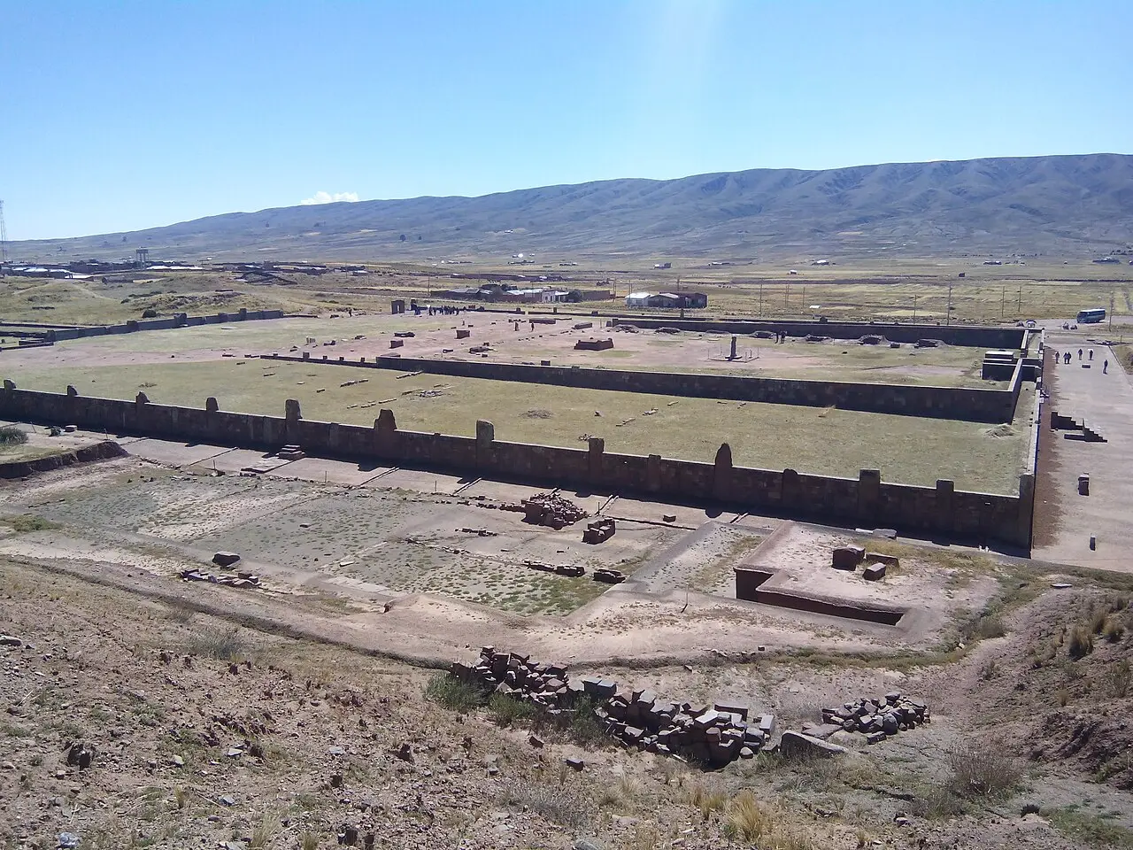 Recinto de pedra de Kalasasaya em Tiwanaku, com muros baixos de blocos verticais em torno de um pátio amplo, e um altiplano com montanhas ao fundo.