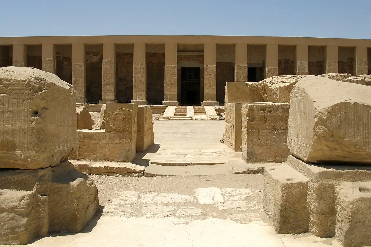 Fachada do Templo de Seti I em Abidos, com pilares quadrados de arenito ao longo de um pórtico e uma escada até a porta, atrás de blocos de pedra gravados.