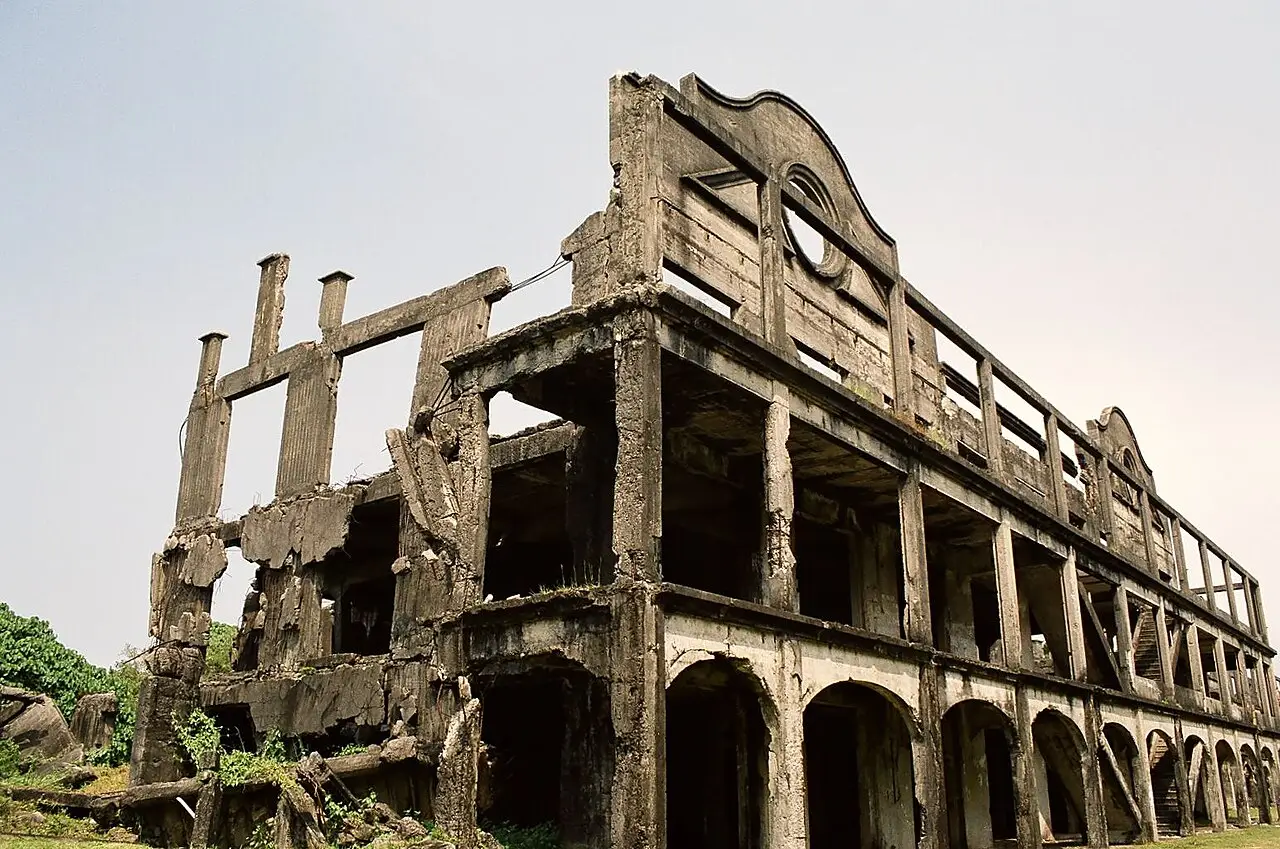 Ruínas de concreto de um quartel de vários andares, com arcos no térreo, vigas expostas e sem telhado, sob céu cinzento, na ilha de Corregidor.