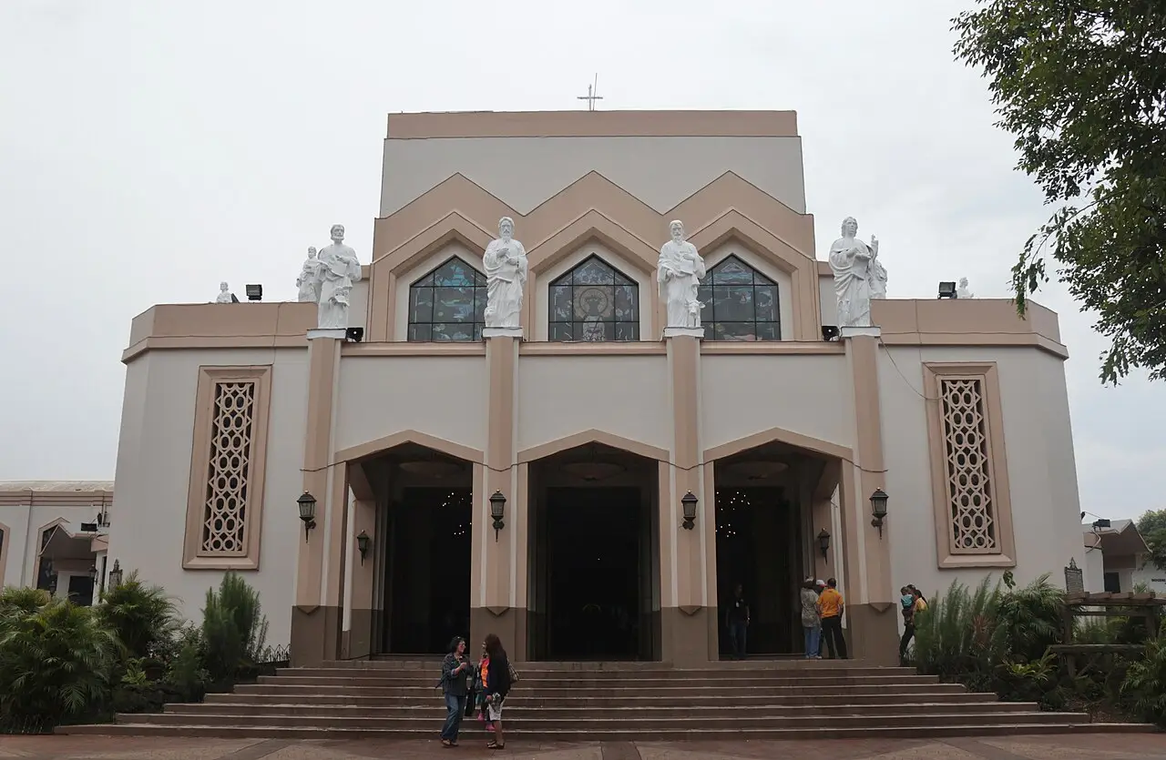 Fachada da catedral de Antipolo, com estátuas brancas no alto, três portas em arco, escadaria na frente e algumas pessoas conversando na entrada.
