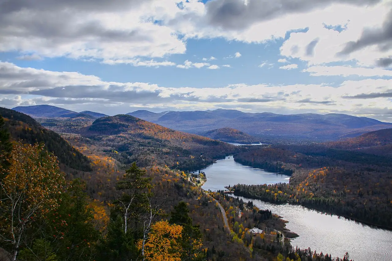 Vista de um mirante sobre colinas com folhagem de outono em amarelo e laranja, um lago comprido no vale e montanhas azuladas ao fundo, em Mont-Tremblant.